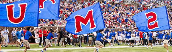 Exciting SMU football game as students enthusiastically run with large SMU flags.